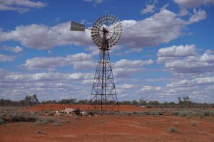 A windmill stands in the desert with blue skies and clouds in the background